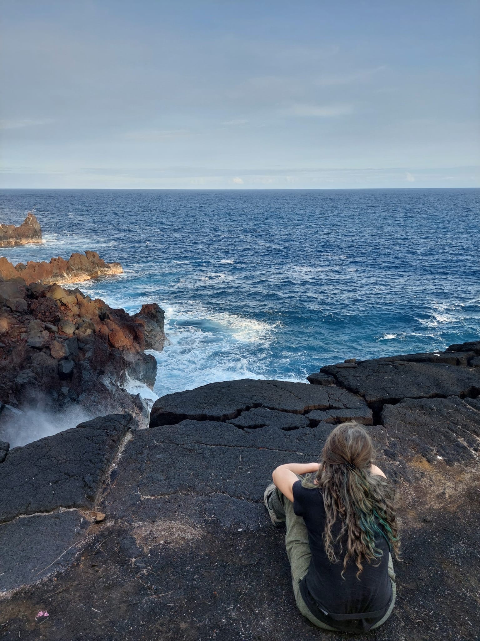 Aoife sitting on volcanic rock looking out at the Hawaiian ocean